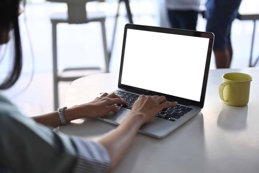 Image shows a young woman's hands on a laptop keyboard.